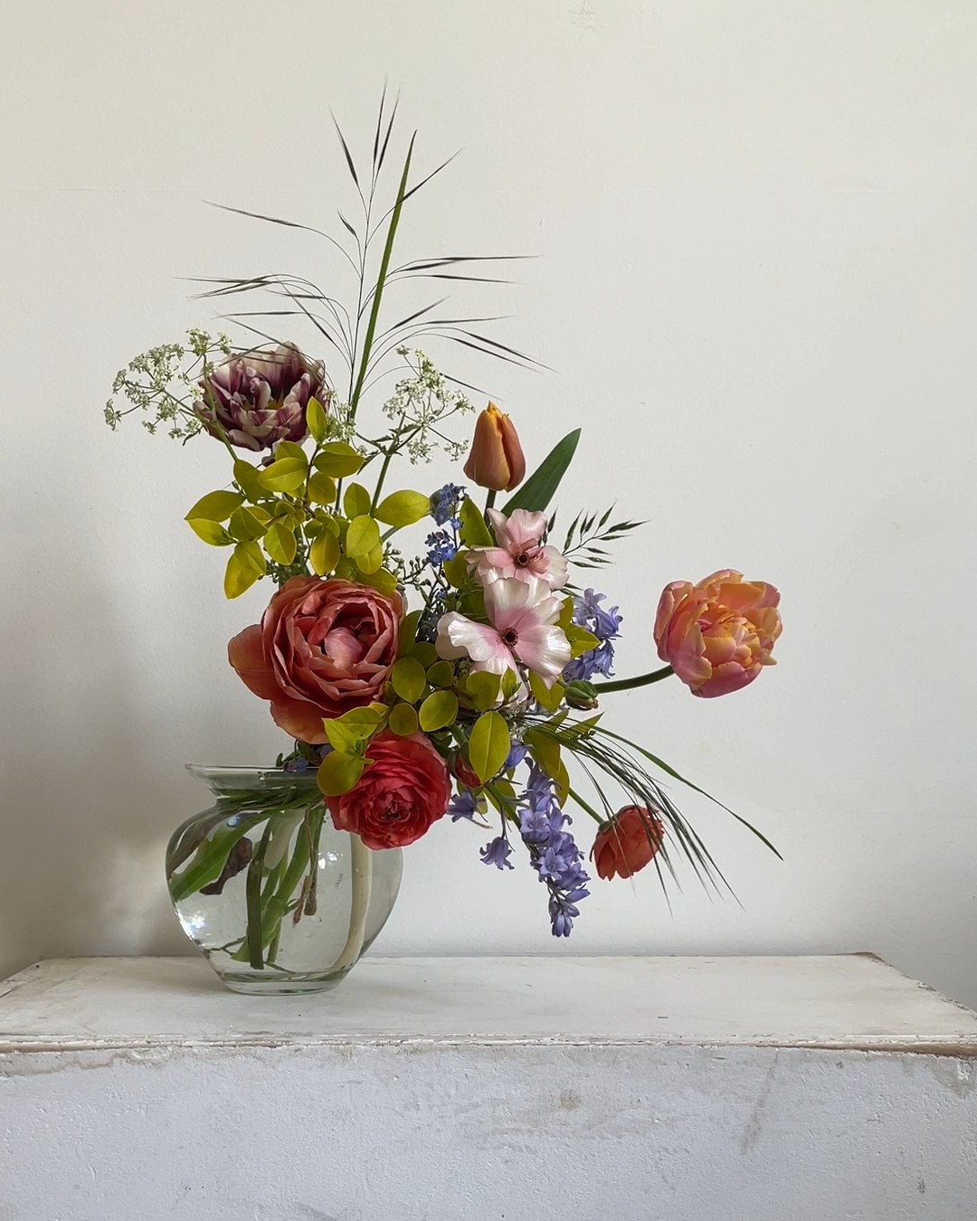 A late spring gift boquet of jewel toned blooms. Ranunculus, double and single tulips, bluebells and a touch of grass. By Mora, a sustainable, season-led event florist based in Hackney, East London