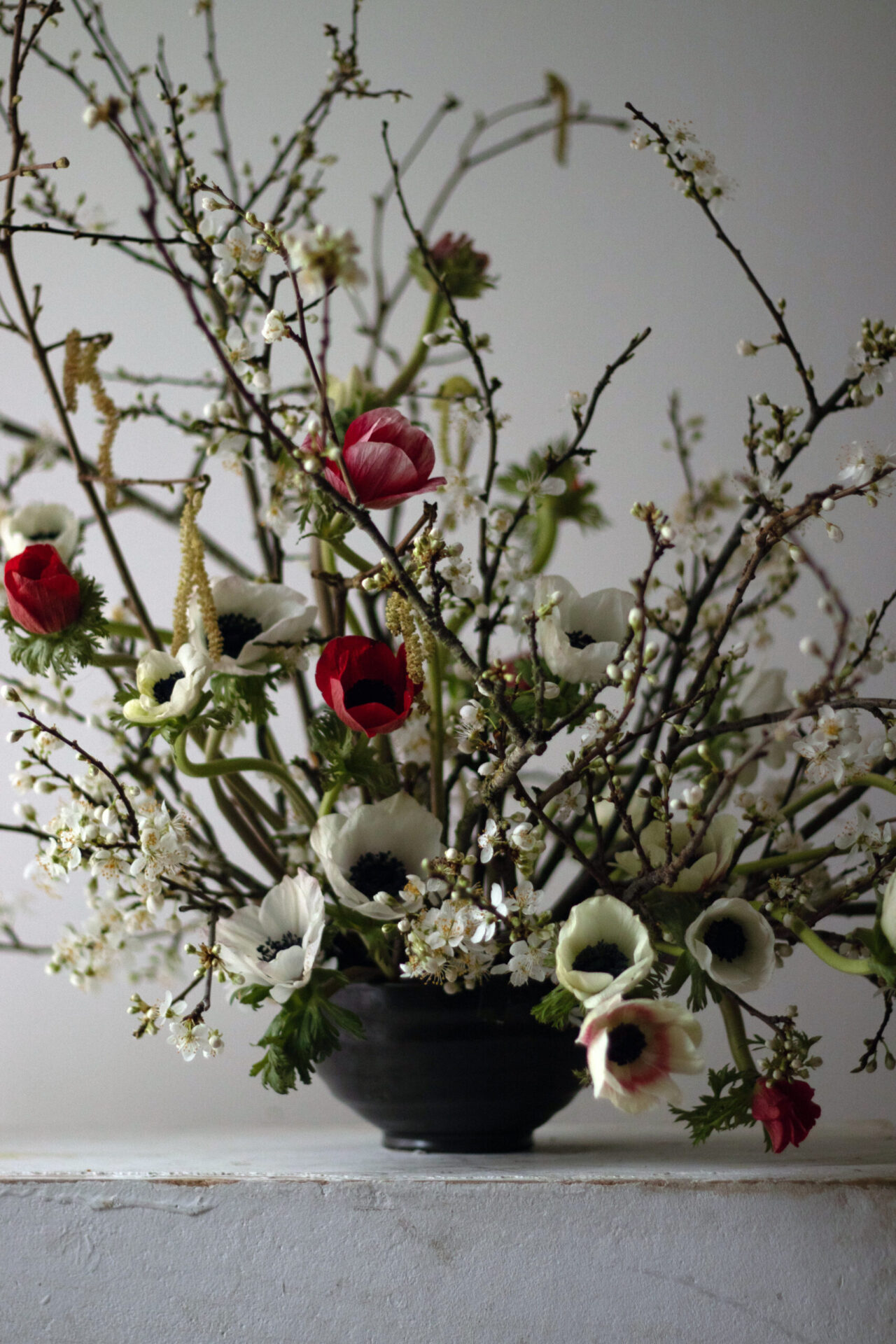 A late winter centrepiece of white and red anemones, hazel catkins and blossom branches. By Mora, a sustainable, season-led event florist based in Hackney, East London