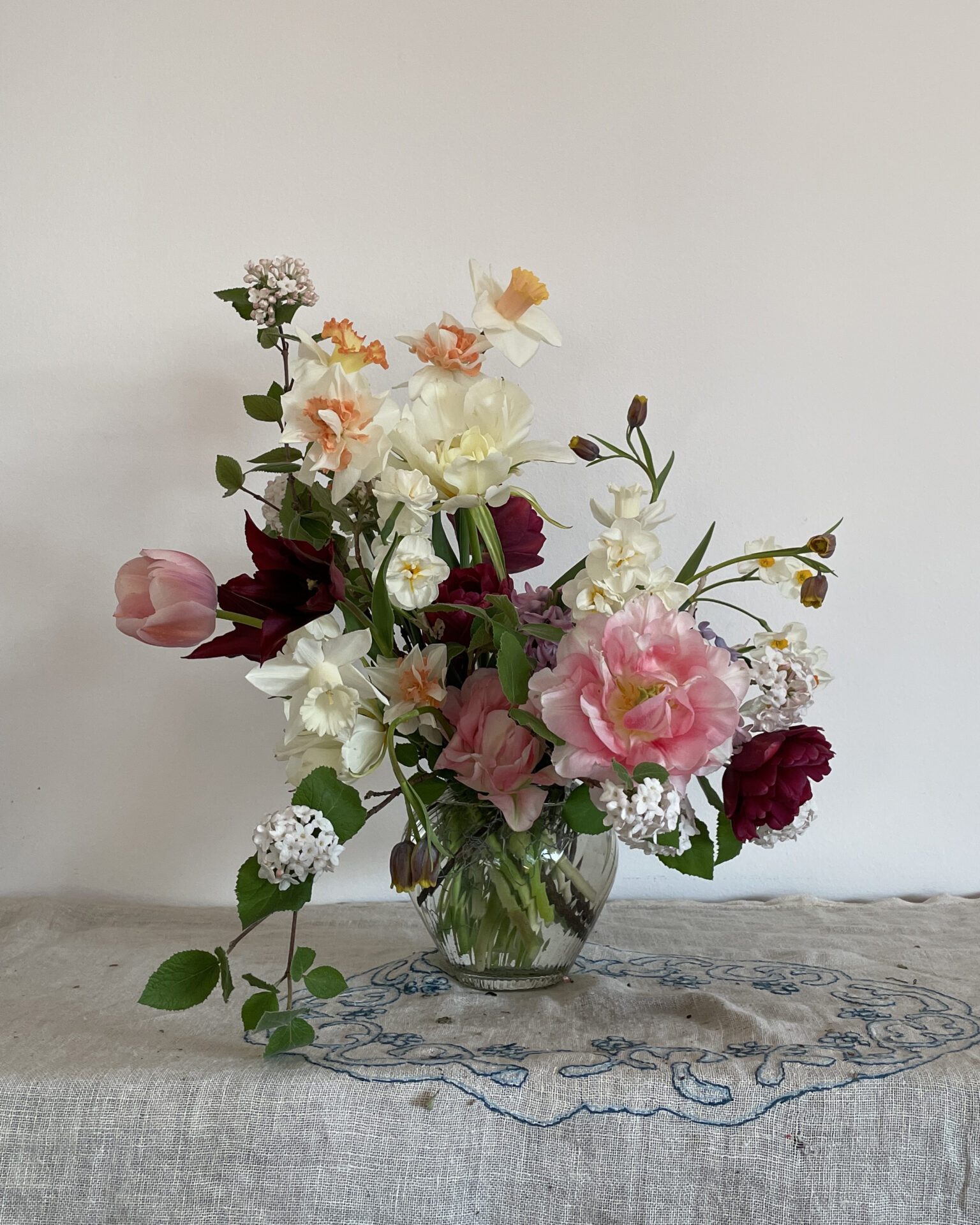 A mid-spring vase of field blooms: double and single tulips, narcissi and fritillarias in elegant tones of cream, burgundy and pink.  By Mora, a sustainable, season-led event florist based in Hackney, East London.