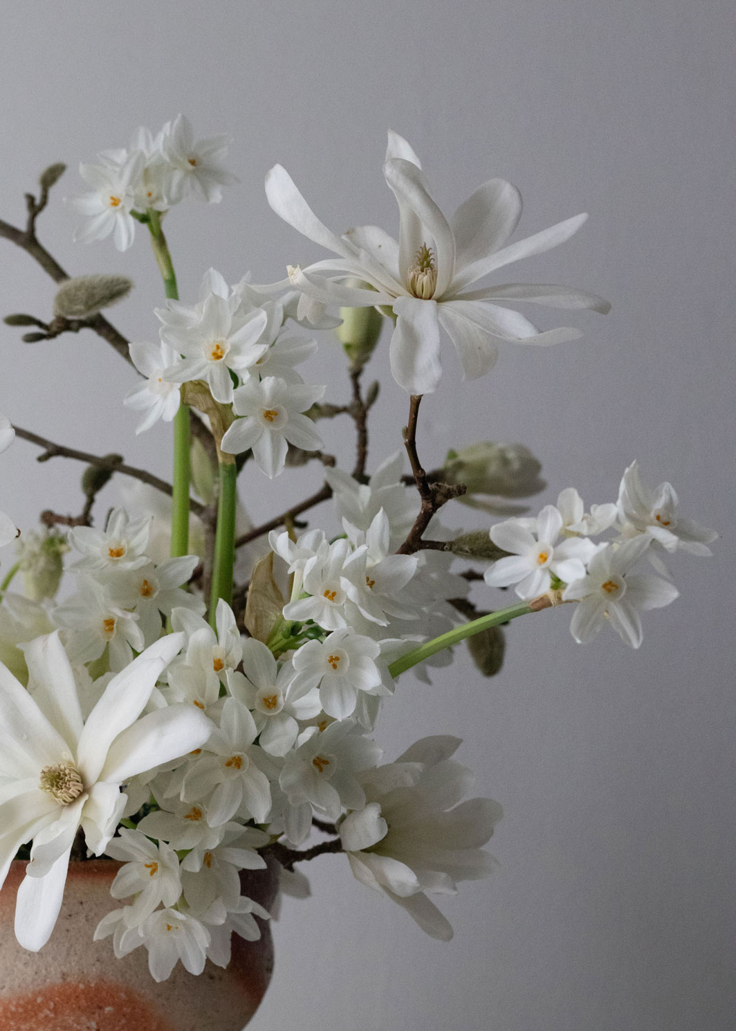 A late winter table arrangement of magnolia stellata branches, paperwhite narcissi and white muscari. By Mora, a sustainable, season-led event florist based in Hackney, East London