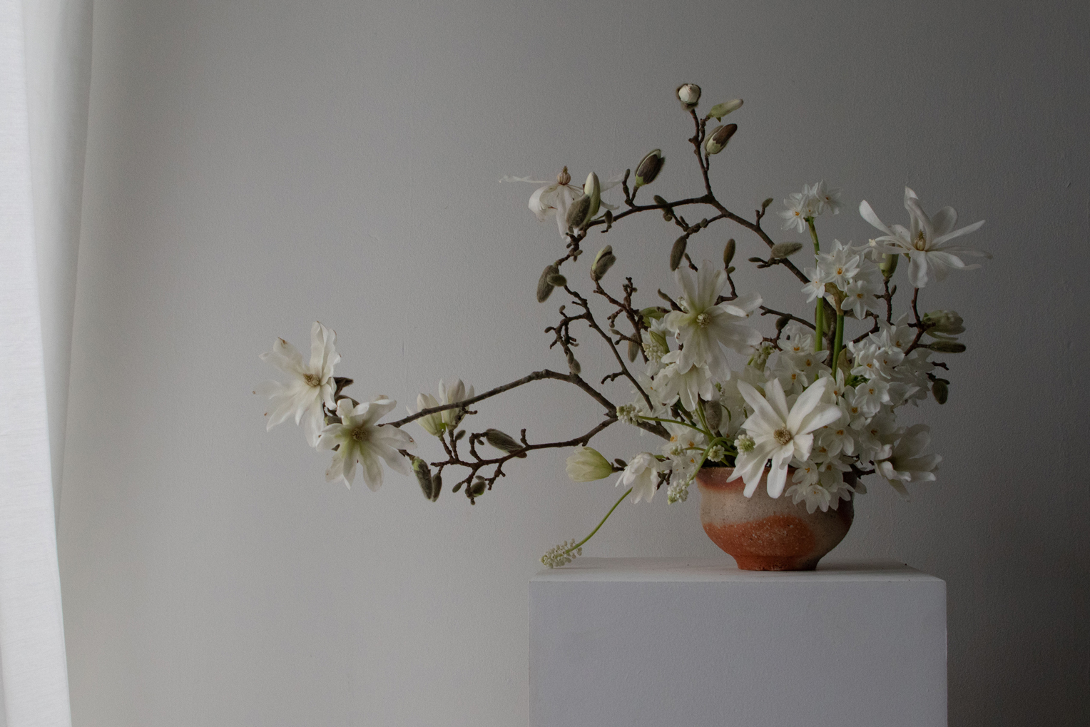 A late winter table arrangement of magnolia stellata branches, paperwhite narcissi and white muscari. By Mora, a sustainable, season-led event florist based in Hackney, East London