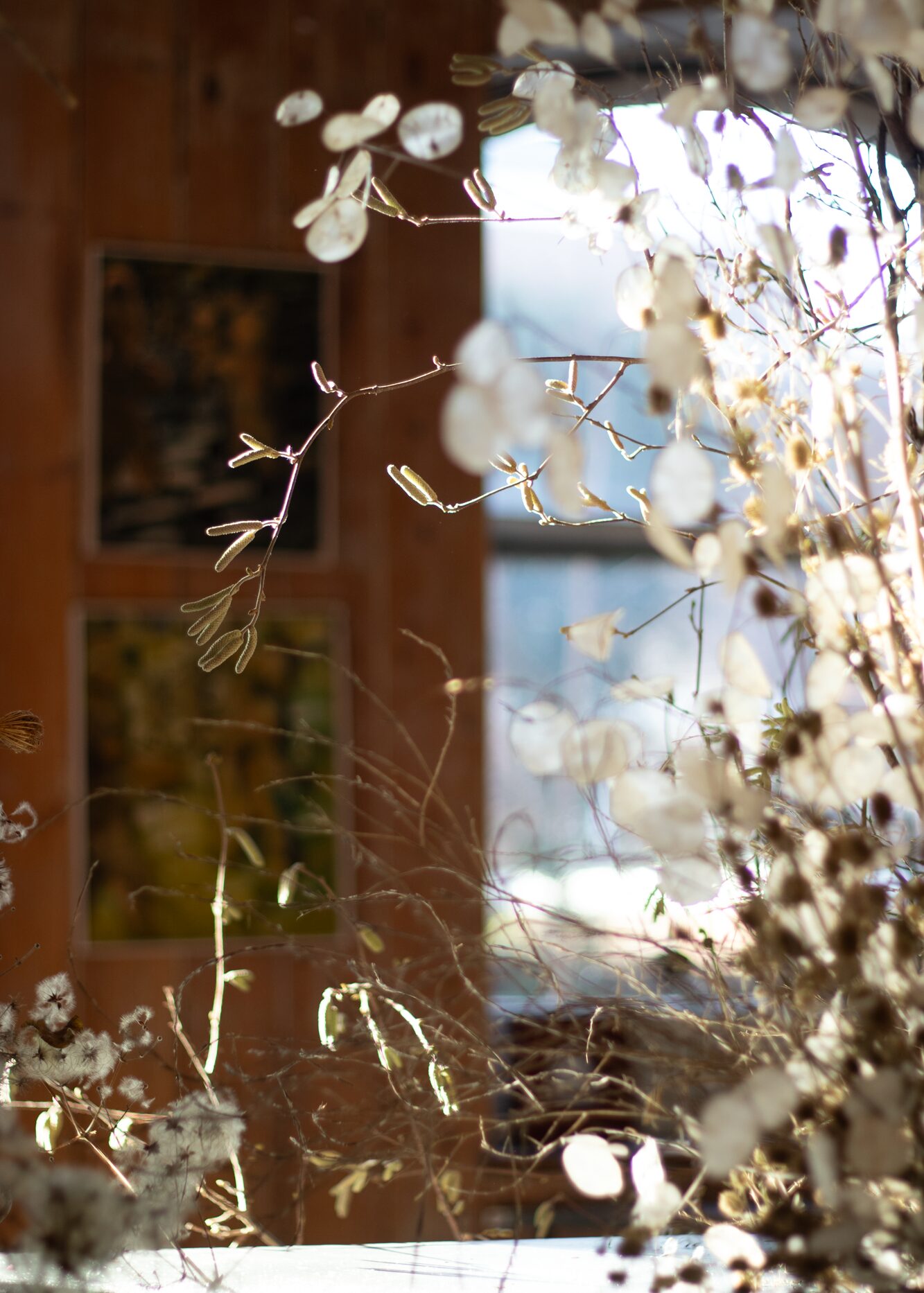 A sculptural winter scene. In the crisp light of the day, the layered display felt calm and airy. Once the sun had set, it would come to life. The tall teasels and skinny hazel branches would draw dramatic silhouettes and bold shadows, whilst the pearly lunaria discs and fluffy clematis seed heads would glow softly in the flickering candlelight. By Mora, a sustainable, season-led event florist based in Hackney, East London